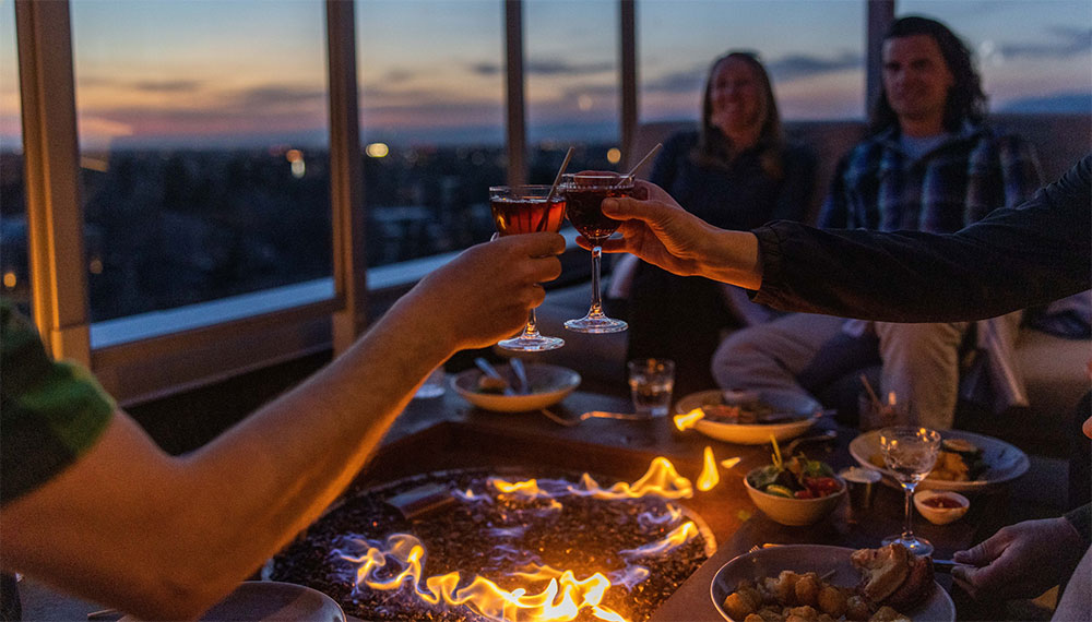 People sitting around a fire pit toasting drinks